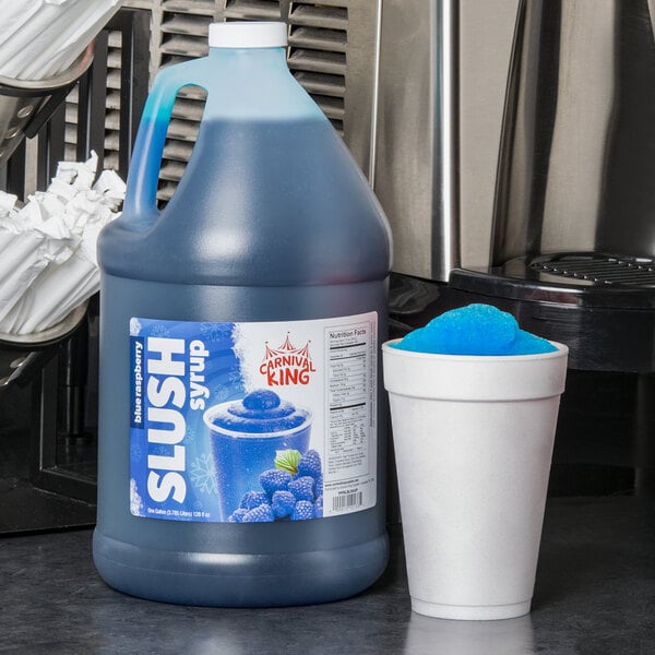 A blue jug of Carnival King Blue Raspberry slushy syrup next to a cup of blue slushy.