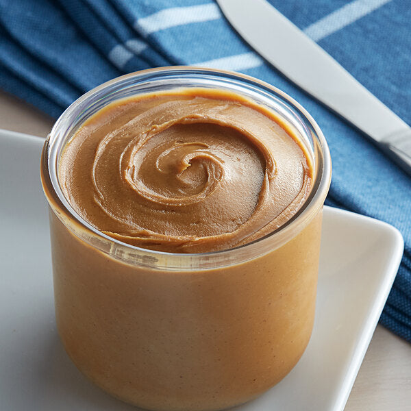 A close-up of a jar of creamy peanut butter on a plate.