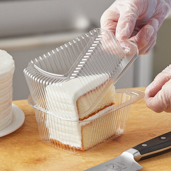 A hand wearing a plastic glove using a knife to cut a slice of cake and place it in a Choice clear plastic container.