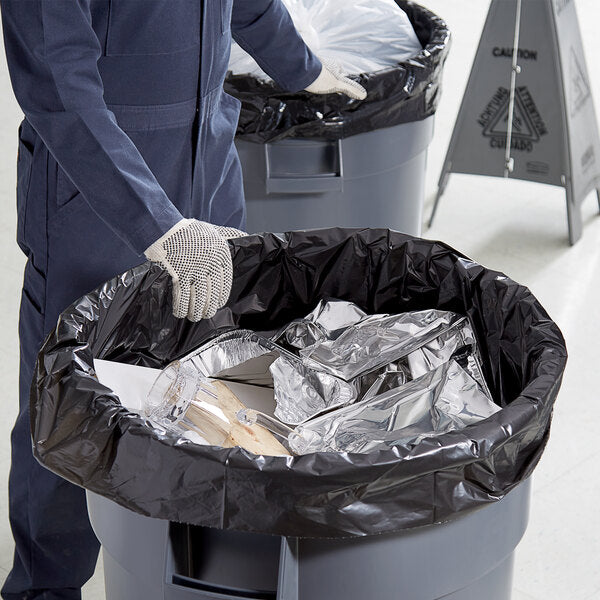 A person wearing gloves and holding a black trash bag