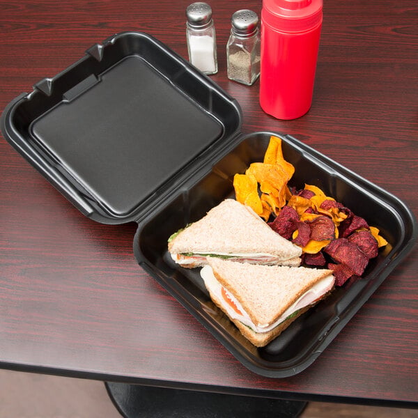 A black Genpak foam container with a sandwich and chips inside.