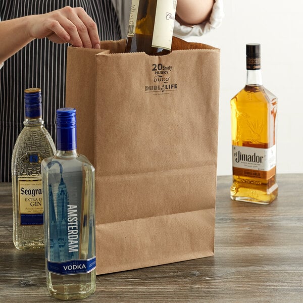A woman putting a bottle of alcohol into a Duro brown paper bag.