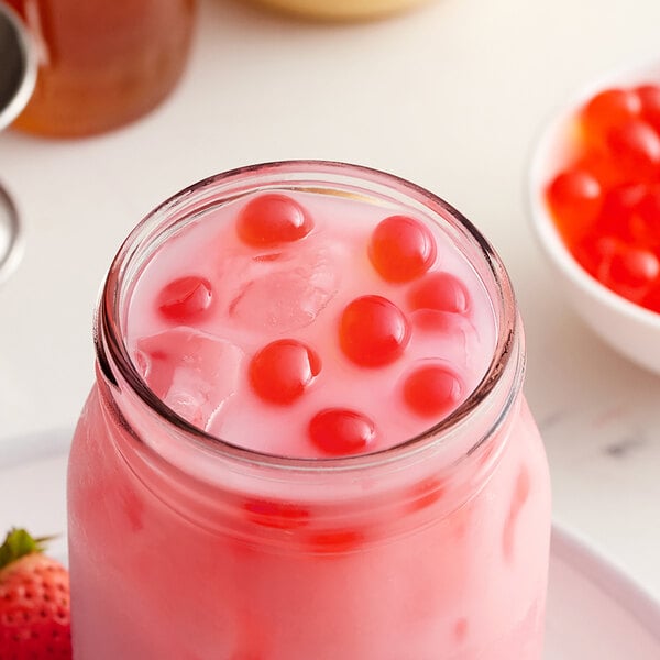 A glass jar filled with pink liquid and Bossen Pure25 Strawberry Bursting Boba with red berries.