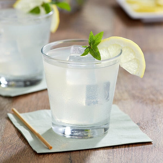A glass of Del Destino lemon juice with ice and a lemon wedge.