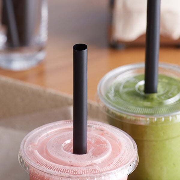 Two plastic cups with Choice black straws on a table with pink drinks.