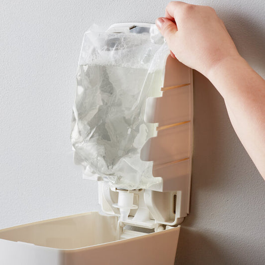 A hand holding a plastic bag of Noble Chemical Novo Pro Series E2 foaming hand soap over a white container.