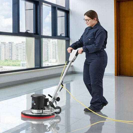 A woman in a blue uniform using a Lavex single speed rotary floor cleaning machine on the floor.
