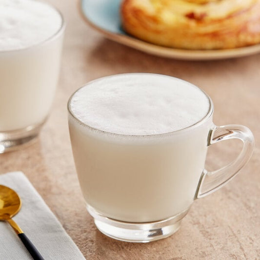 A white glass mug of milk with a spoon in it.