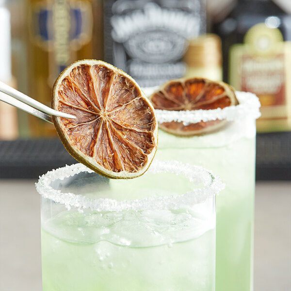 A pair of white tweezers holding a dried lime slice over a glass of water.