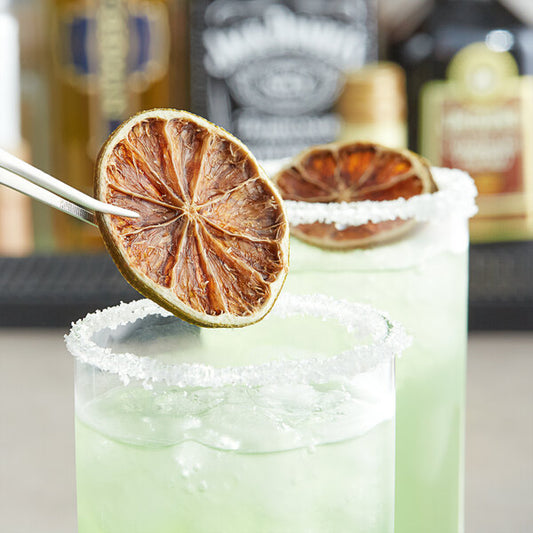 A pair of white tweezers holding a dried lime slice over a glass of water.