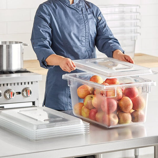 A woman in a chef's uniform holding a Vigor clear polycarbonate food storage container full of apples.