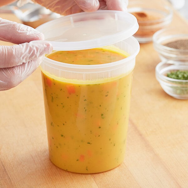A gloved hand puts a plastic lid on a ChoiceHD translucent plastic deli container of soup.