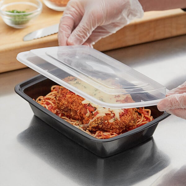 A person in plastic gloves holding a black rectangular plastic container filled with food.