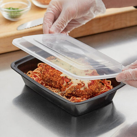 A person in plastic gloves holding a black rectangular plastic container filled with food.