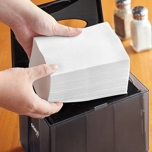 A person holding a box of white OneUp by Choice dispenser napkins.