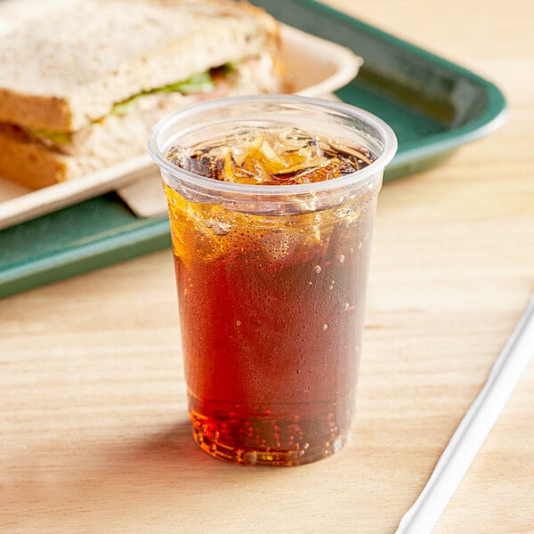 A plastic cup with a drink in it next to a sandwich.