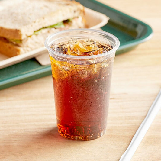A plastic cup with a drink in it next to a sandwich.