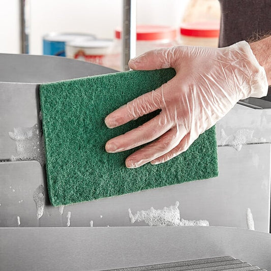 A person in gloves cleaning a metal surface with a dark green Lavex scouring pad.