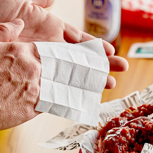 A person using a Choice lemon-scented moist towelette to clean their hands over a plate of food in a pizza parlor.