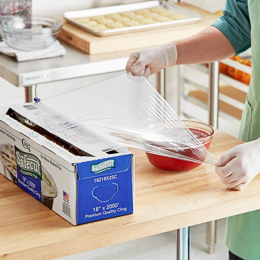 A woman in a green shirt and gloves using a slide cutter to wrap a bowl of red liquid with Choice Safecut premium foodservice film.