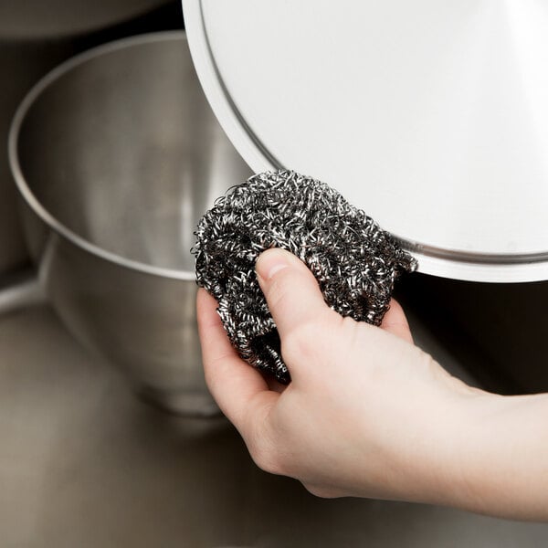 A hand holding a 3M Scotch-Brite stainless steel scrubber.